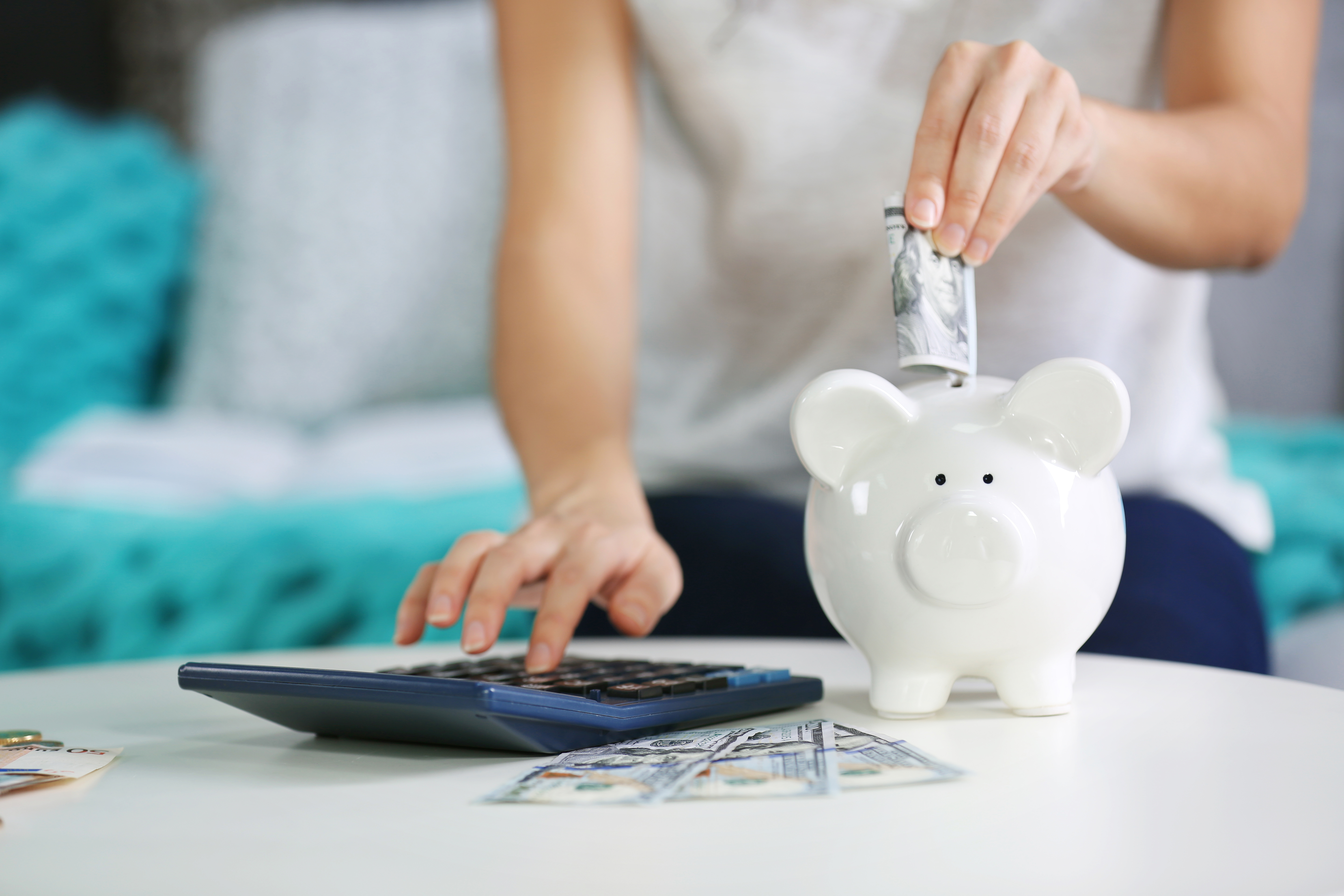 Woman's hand putting money into piggy bank and using calculator